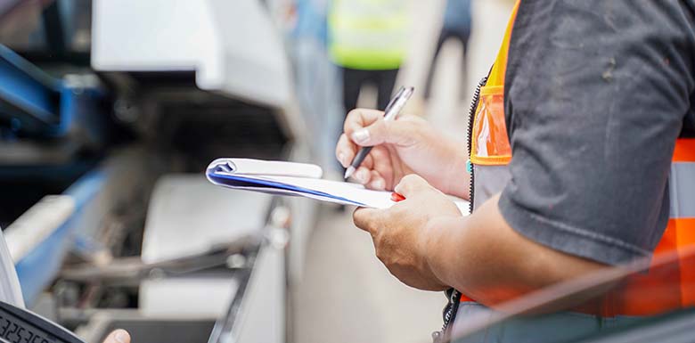 Person filling out papers while examining damaged car